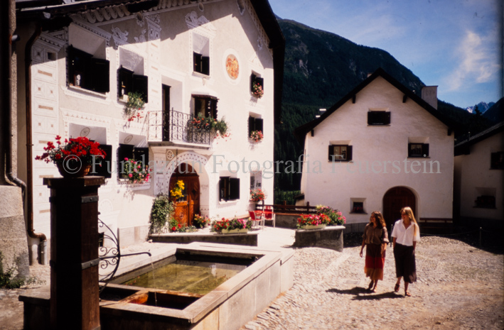 Zwei Frauen auf Dorfplatz bei Brunnen und Haus, Fassade mit Sgraffito