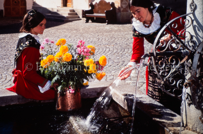Zwei Frauen in Trachten mit Blumen bei Brunnen