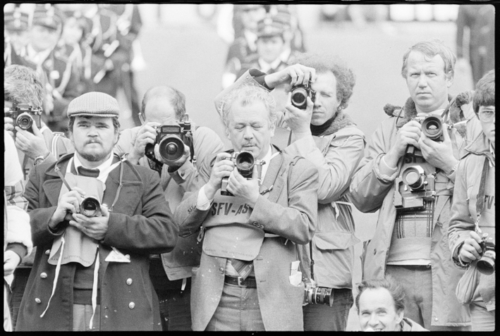 Mehrere Fotografen mit Apparaten, hinter ihnen Fussballplatz und Blasmusikanten