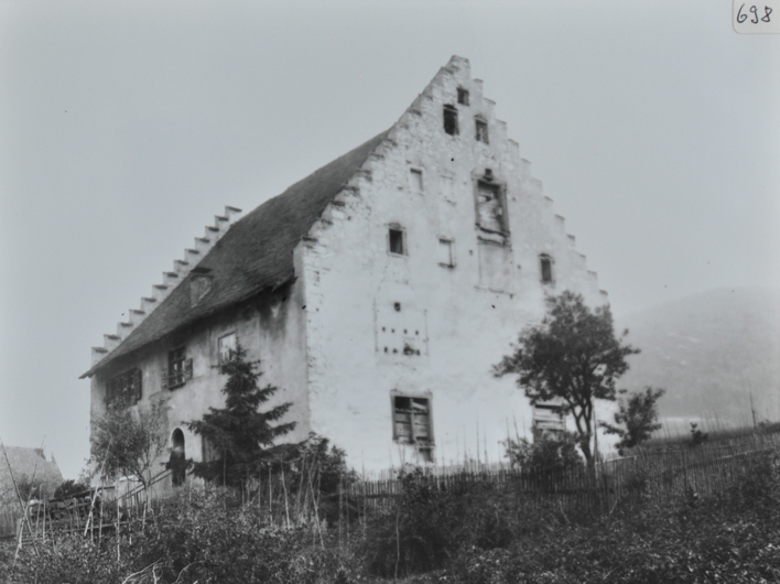 Mehrstöckiges gemauertes Wohnhaus mit Satteldach, Gebäude nicht fertig gebaut, Holzbälken verschliessen die Fenster, um das Haus Wiese mit Gebüsch