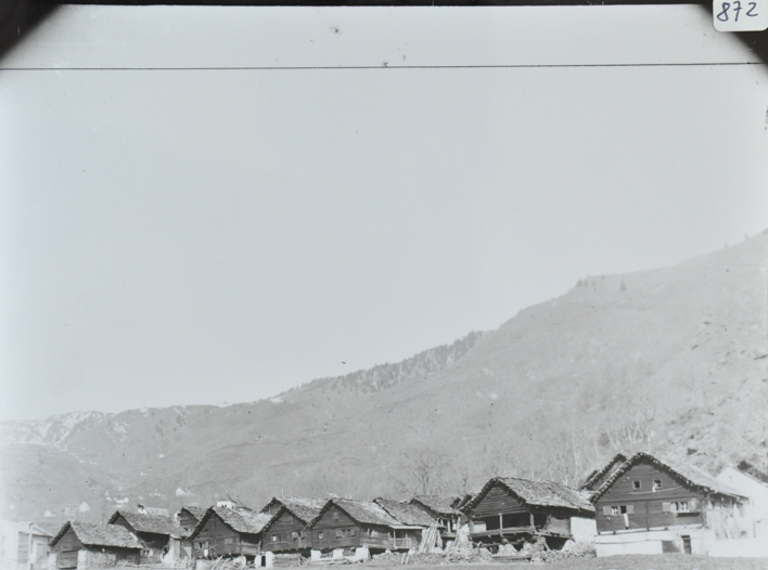 Ansicht des Dorfes mit mehreren Wohnhäusern, Häuser aus Holz mit gemauerten Fundament, Satteldächer, Bergkette im Hintergrund