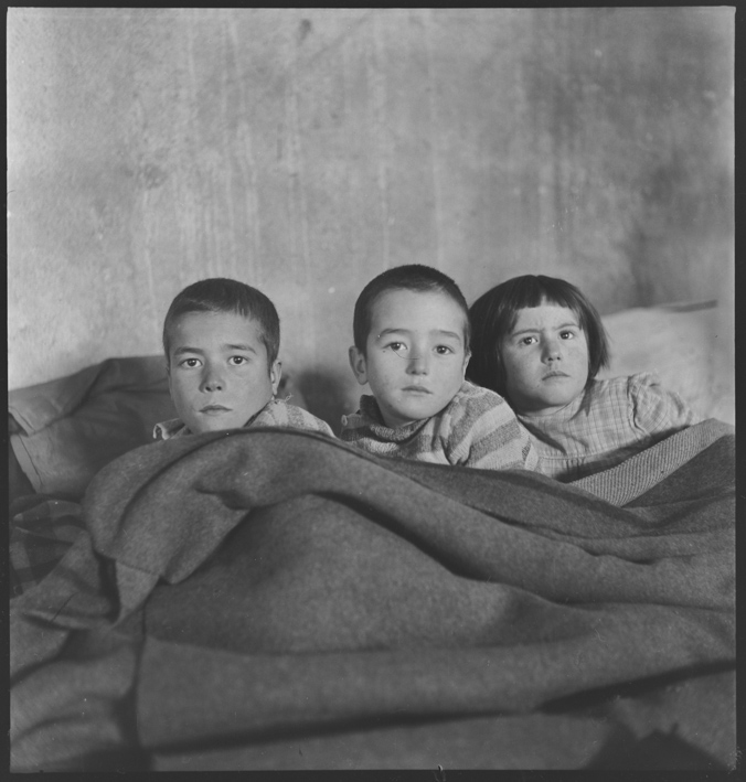Drei Kinder im Bett liegend in einer Baracke