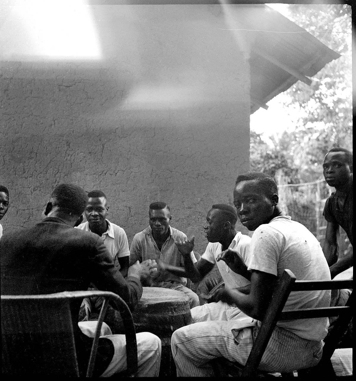 Belgisch-Kongo, Leopoldville (Kinshasa): Menschen; Mehrere farbige Männer sitzen im Kreis und spielen auf einem Tam-Tam (Trommel)