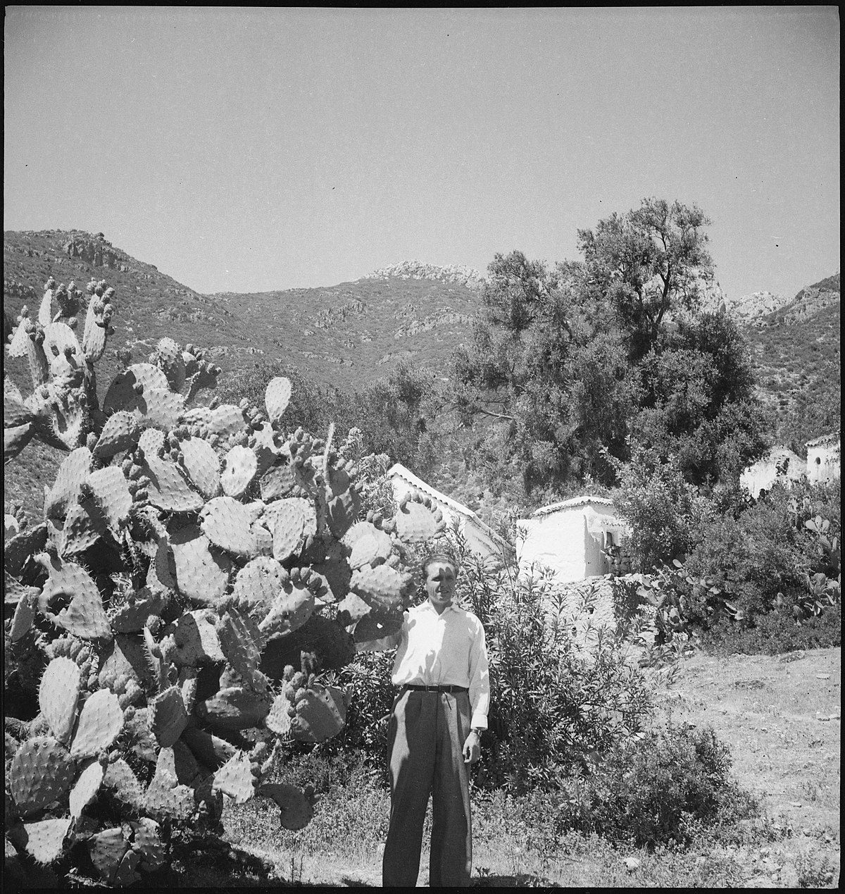 Spanisch-Marokko, Tétouan: Claude Clarac; Claude Clarac stehe neben einer grossen Kaktuspflanze vor einem mit Büschen verdecktes Gebäude an einem felsigen Berghang
