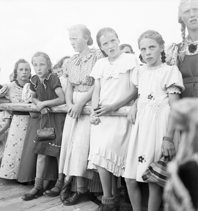 Gruppe von Mädchen in Sommerkleidern hinter einer Abschrankung 