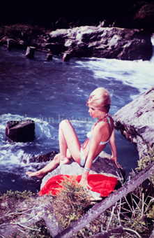 Frau in Badekleidung am Wasser auf Stein