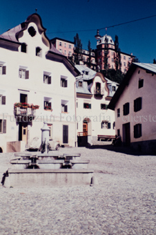 Dorfplatz mit Brunnen und Häuser mit Anschrift «Colonials»