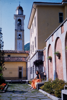 Frau auf Treppe vor Haus im Tessin mit Kirchturm