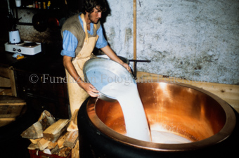 Käser giesst Milch in Kupferkessel