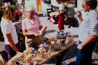Zwei Frauen und ein Mann an Marktstand mit Holztieren