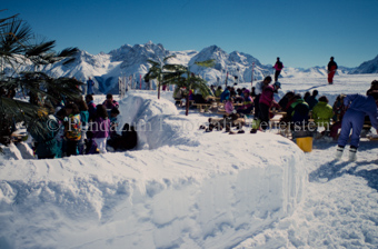 Personen an Tischen im Schnee, künstliche Palmen und Kokosnüsse