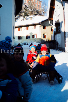 Kinder auf Schlitten, die verschneite Dorfstrasse herab