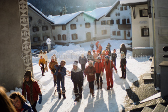 Kinder mit Schlitten beim verschneiten Dorfplatz mit Brunnen