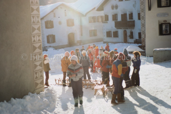 Kinder mit Schlitten beim verschneiten Dorfplatz mit Brunnen