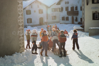 Kinder mit Schlitten beim verschneiten Dorfplatz mit Brunnen