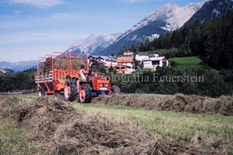 Bauer auf Traktor mit Heuwagen beim Heuaufsammeln