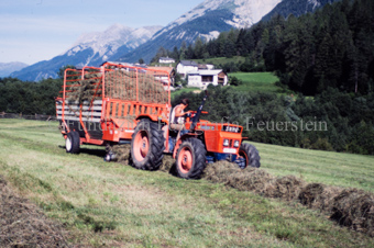 Bauer auf Traktor mit Heuwagen beim Heuaufsammeln