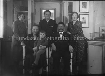 Gruppenaufnahme, Familie im Verkaufsraum im Atelier der Feuersteins, an der Wand gerahmte Fotografien