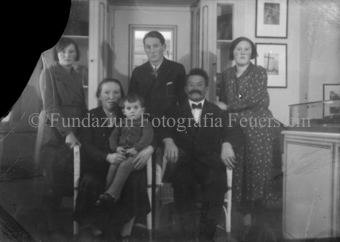 Gruppenaufnahme, Familie im Verkaufsraum im Atelier der Feuersteins, an der Wand gerahmte Fotografien, unscharf