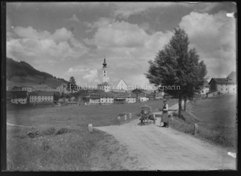 Mann mit Kuh und Wagen, im Hintergrund Ftan
