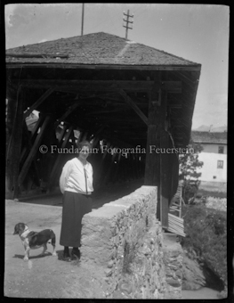 Frau mit Hund steht vor einer Brücke