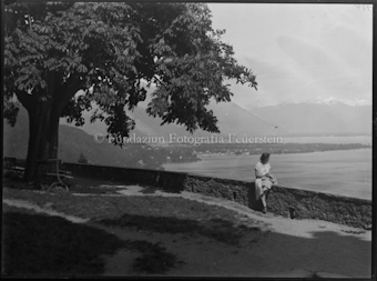Frau auf Mauer sitzend, im Hintergrund der Lago Maggiore