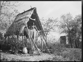 Hütte im Stil der Pfahlbauer, im Hintergrund ein turmartiges Gebäude