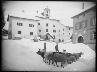 Schafe, Schäfer und Hund um Brunnen auf verschneitem Dorfplatz