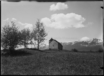 Blick auf kleine Kapelle mit Bäumen auf Wiese, Berggipfel im Hintergrund