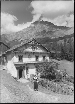 Frau vor Wohnhaus, Berg im Hintergrund