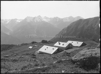 Drei Häuser auf Alp; Berge im Hintergrund
