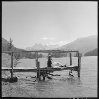 Frau auf Steg sitzend an Seeufer