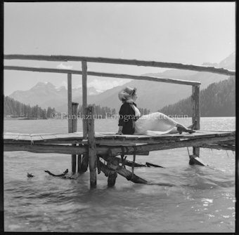 Frau auf Steg sitzend an Seeufer