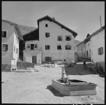 Dorfplatz mit Brunnen und Wohnhäusern