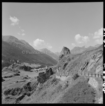 Strasse an Fels, entfernt sichtbares Dorf 