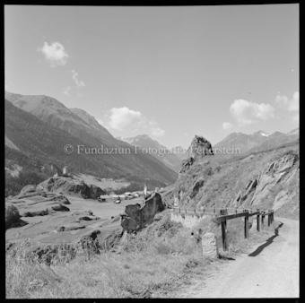 Strasse an Fels, entfernt sichtbares Dorf 