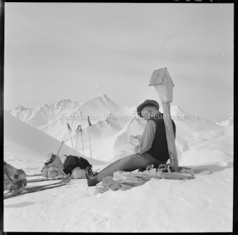 Mann sitzt an Wegeskreuz, Rucksäcke und Stöcke