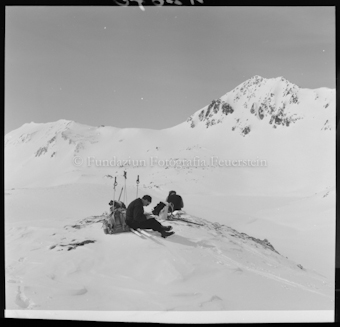 Person mit Ski, Stöcken und Rucksäcken sitzend