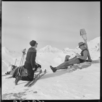 Zwei Personen mit Ski, Stöcken und Rucksäcken