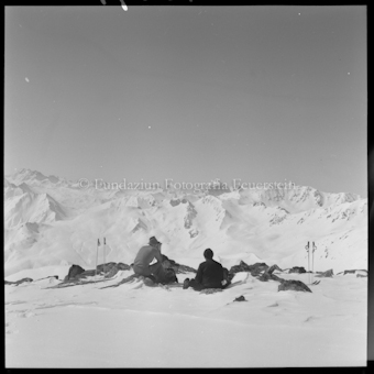 Zwei Personen mit Ski, Stöcken und Rucksäcken