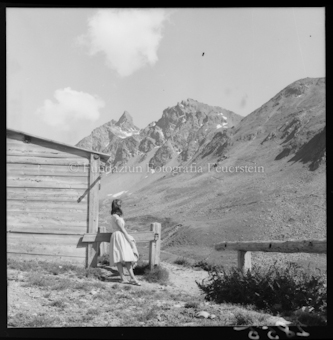Frau vor Berghütte, Berge im Hintergrund