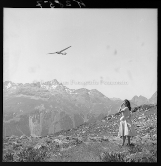 Segelflieger über Berglandschaft; Frau auf Wiese
