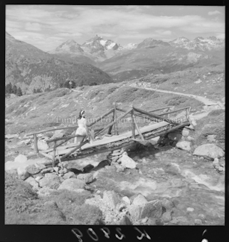 Frau auf Holzbrücke vor Bergen