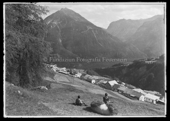 Blick auf Ortschaft, im Vordergrund zwei Jungen auf Heuballen