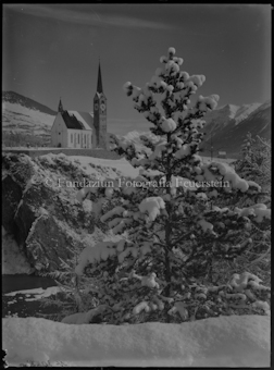 Kirche von Scuol, über den Inn fotografiert, im Vordergrund Tanne, Winter