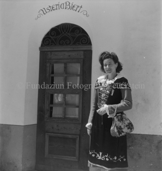 Frau in Tracht mit Handtasche vor Tür