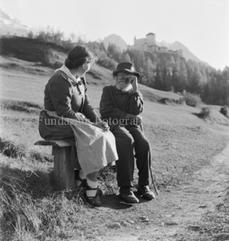 Frau und älterer Mann mit Bart auf Sitzbank, Schloss im Hintergrund