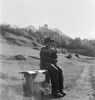 Älterer bärtiger Mann mit Stock auf Sitzbank, Schloss im Hintergrund