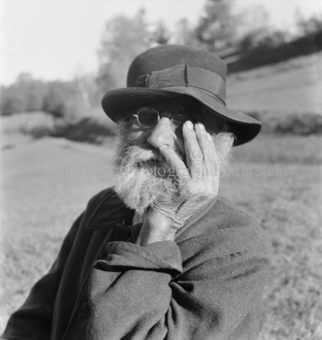 Älterer bärtiger Mann mit Brille und Hut, Hand im Gesicht