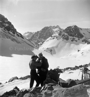 Mann und Frau in verschneiter Berglandschaft, sie richtet ihm den Kragen